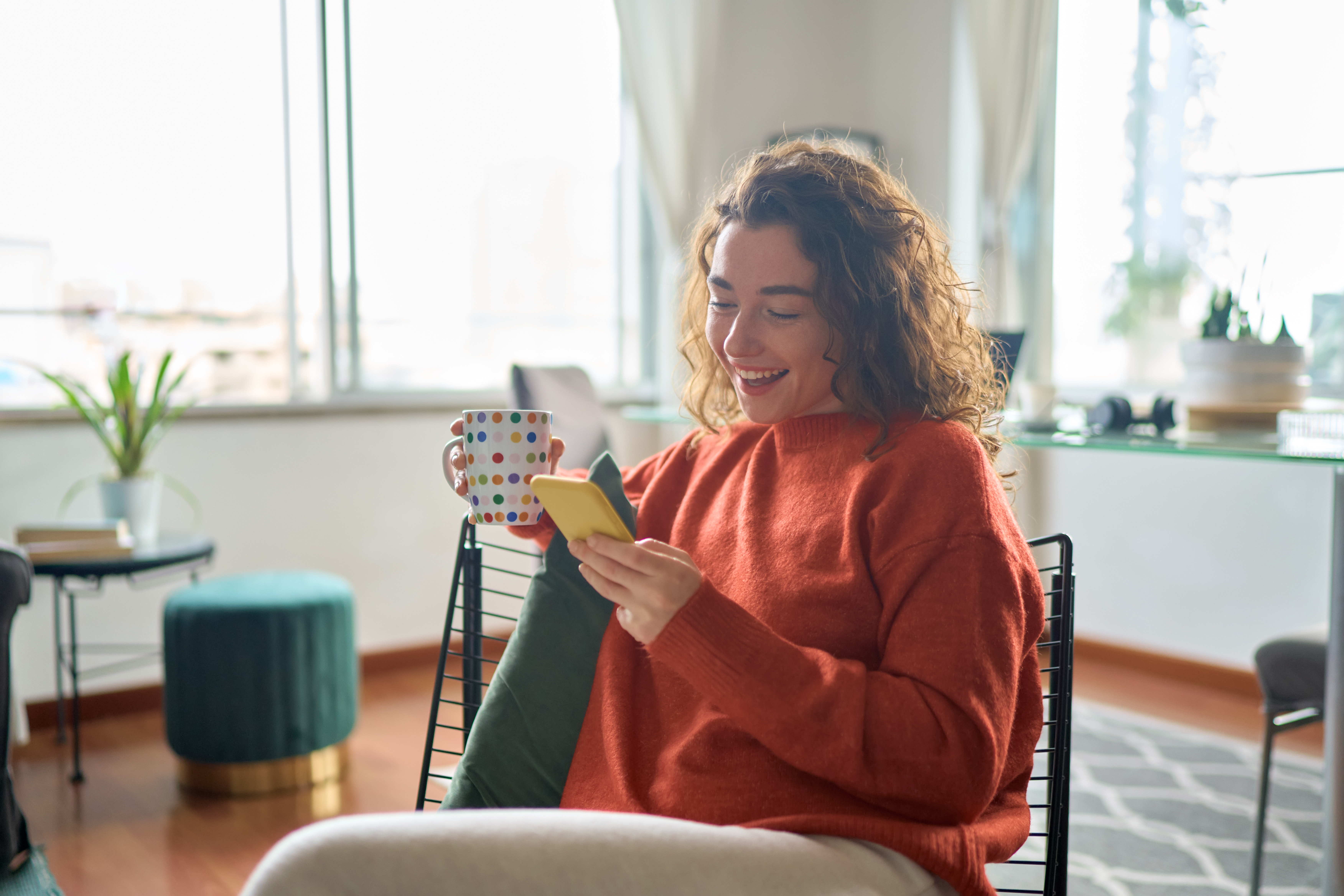 A woman smiles looking at her smartphone and seeing her credit union money market account balance grow.
