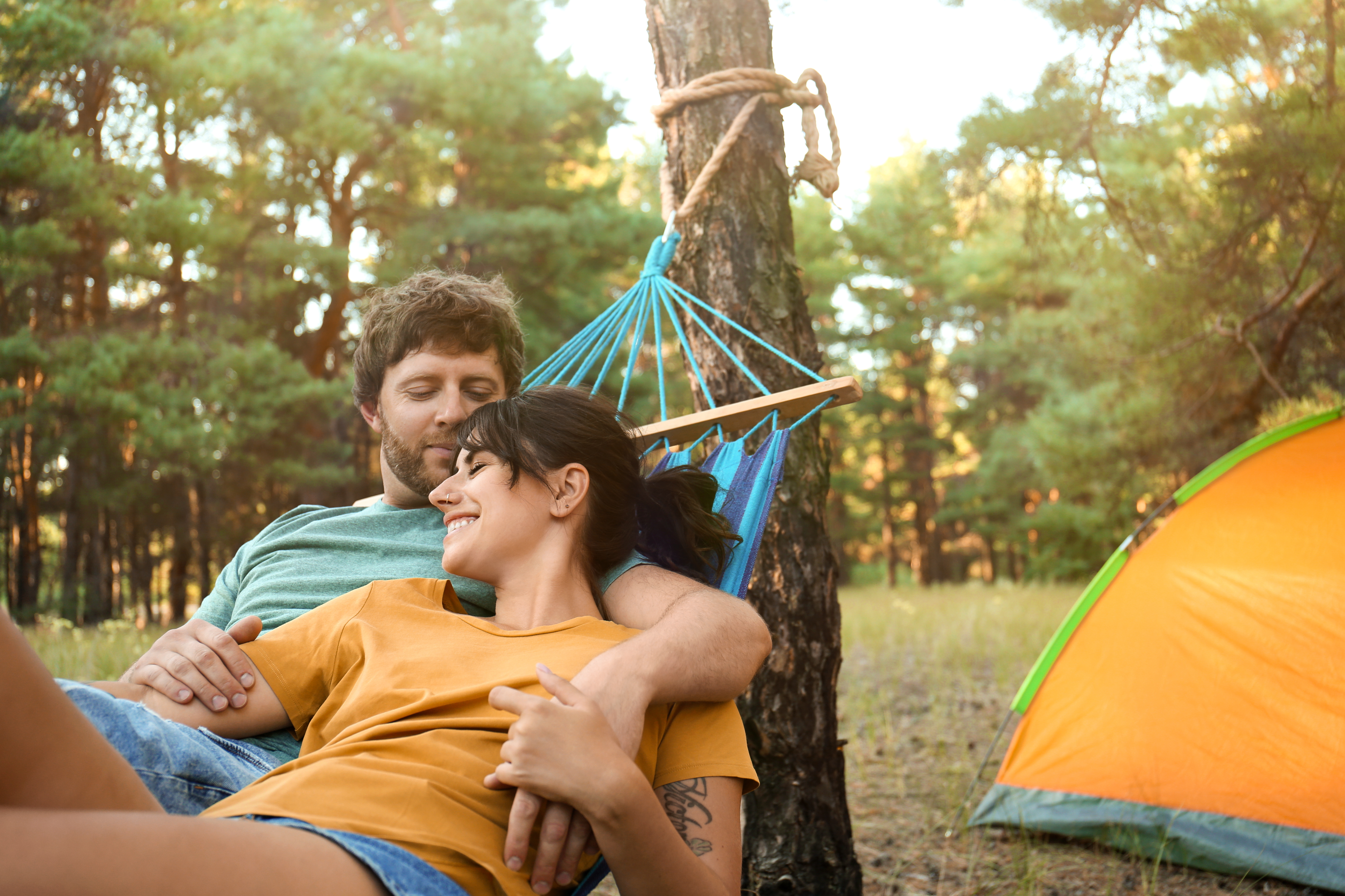 A young couple lay in a hammock together at their campsite
